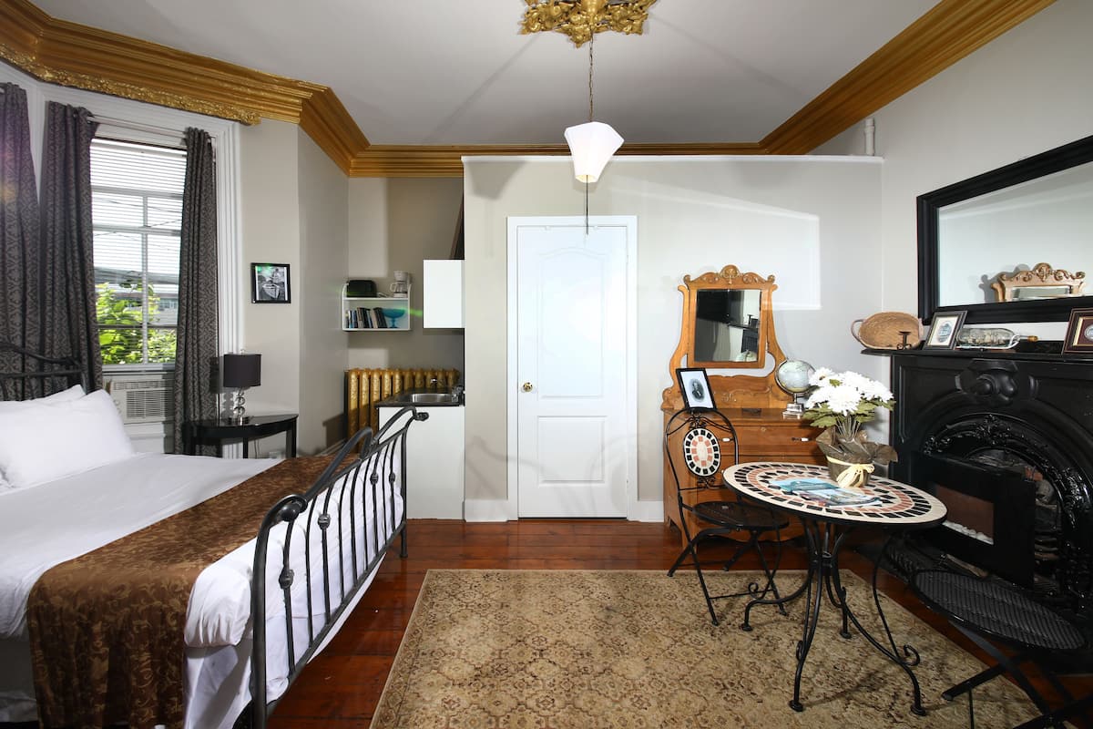 A hotel room with a bed, a desk with a mirror, a dresser, and a fireplace.