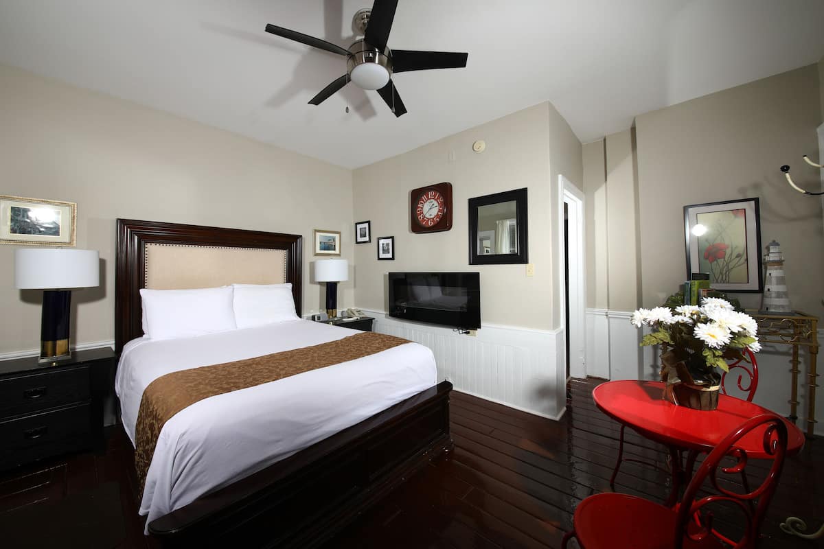 A hotel room with a large bed, a TV, a ceiling fan, a red chair, and a small table with flowers.