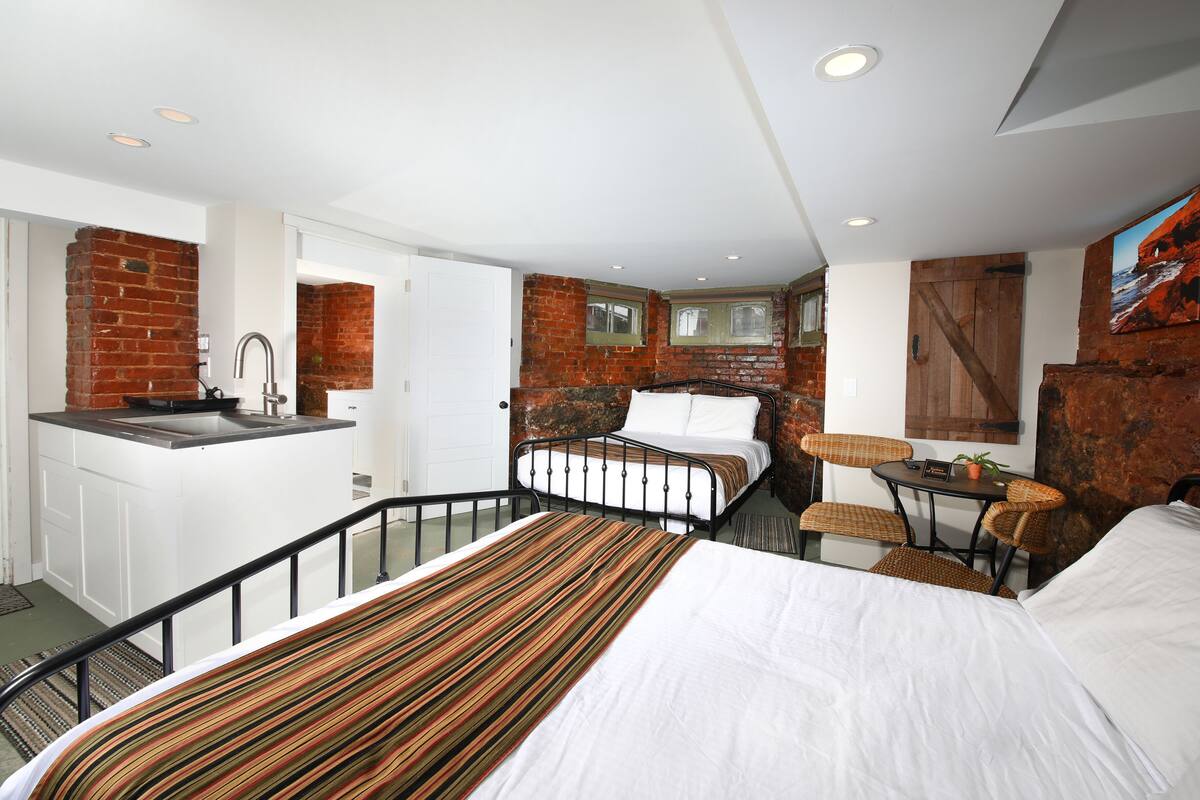 A bedroom with a bed, a small table, a chair, and a view of the outside.