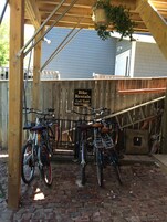 A wooden bike rental station with a sign for bike rentals, a brick ground, and a wooden fence in the background.