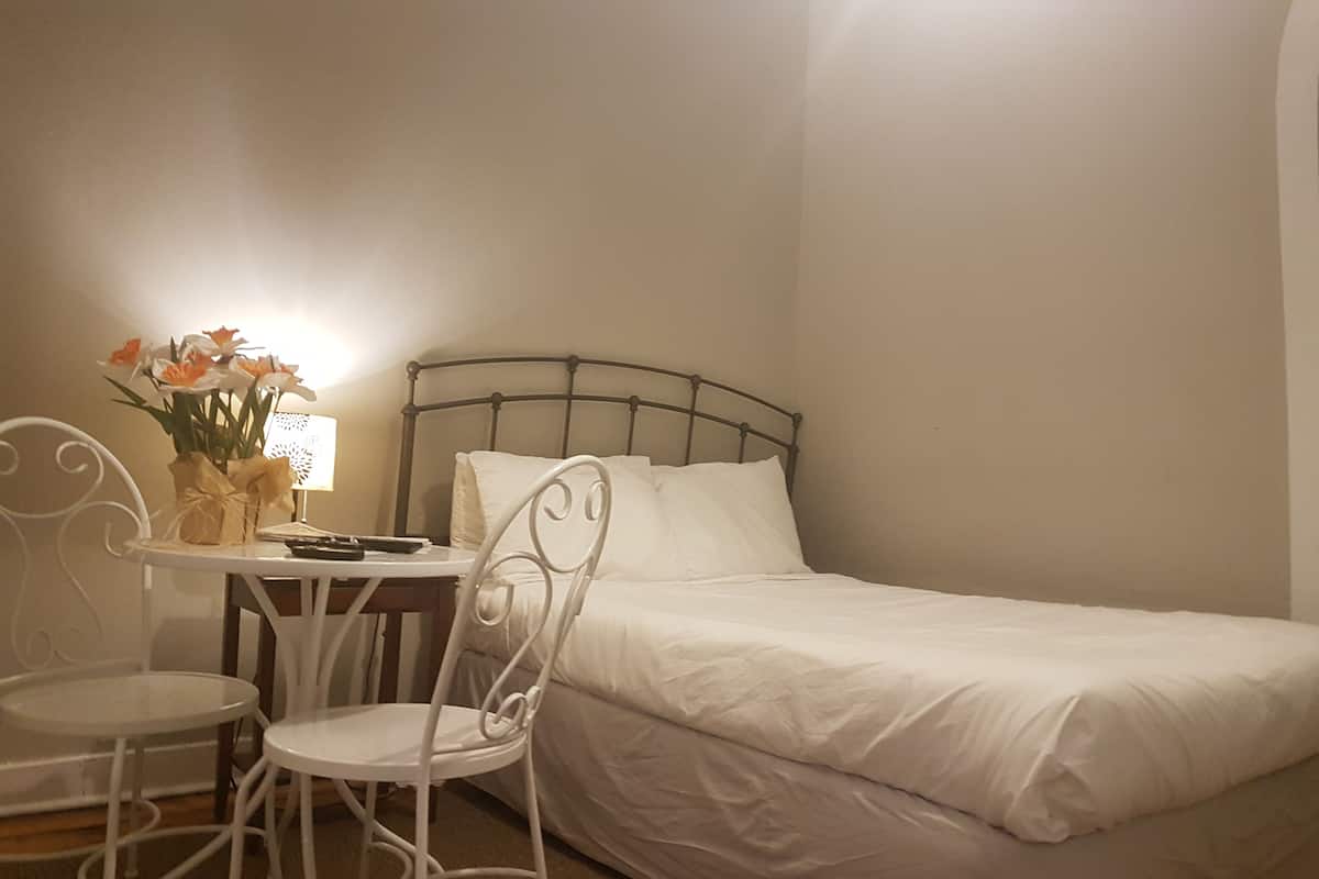 A bedroom with a single bed, a small table with a chair, and a vase with flowers.