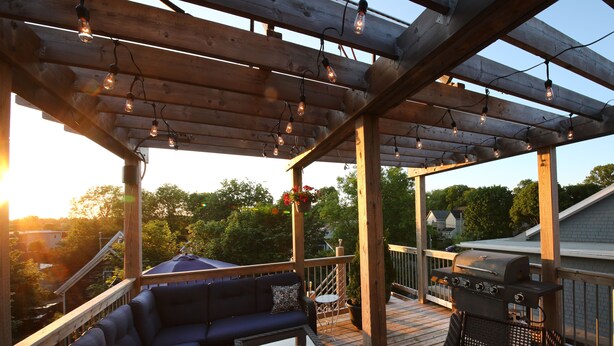 Una terraza techada al aire libre con pérgola de madera, zona de estar y parrilla.