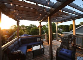 A covered outdoor deck with a wooden pergola, seating area, and barbecue grill.