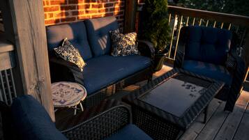 A wooden deck with wicker furniture, including a sofa and chairs, and a small round table.