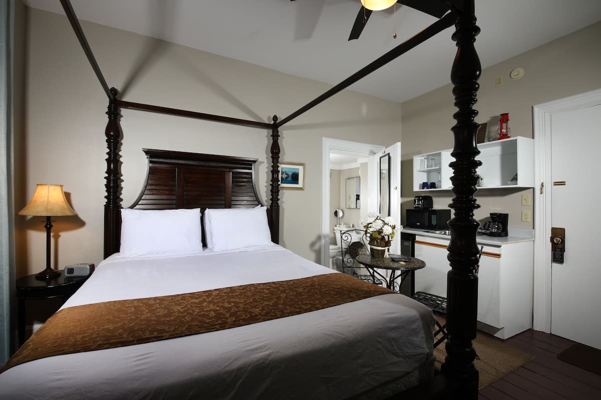 A four-poster bed with a wooden headboard, a bedside table with a lamp, and a small table with a vase of flowers.