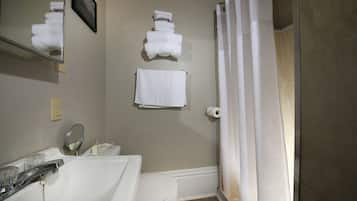 Un baño con lavamanos, inodoro y cortina de ducha. Hay toallas colgadas en la pared y un cuadro enmarcado sobre el espejo.