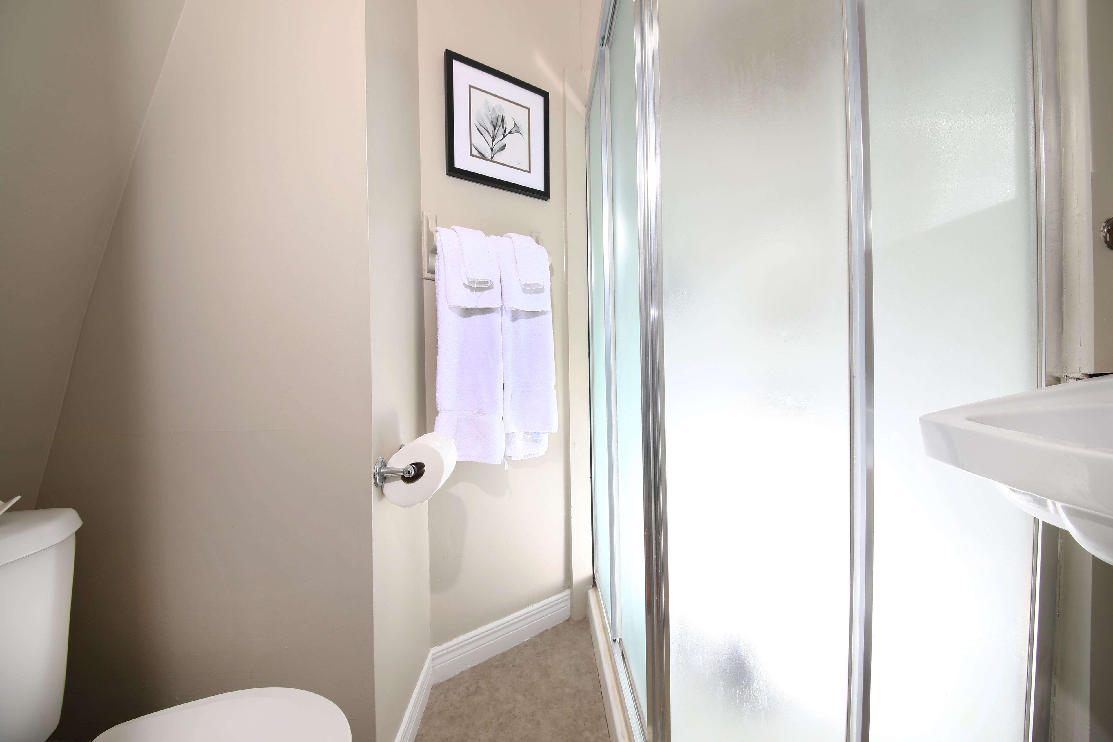 Une salle de bain avec des toilettes, un lavabo et une douche. Deux serviettes blanches sont accrochées au mur.