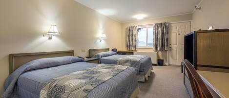 A hotel room with two beds, a television, a desk, and a window with curtains.