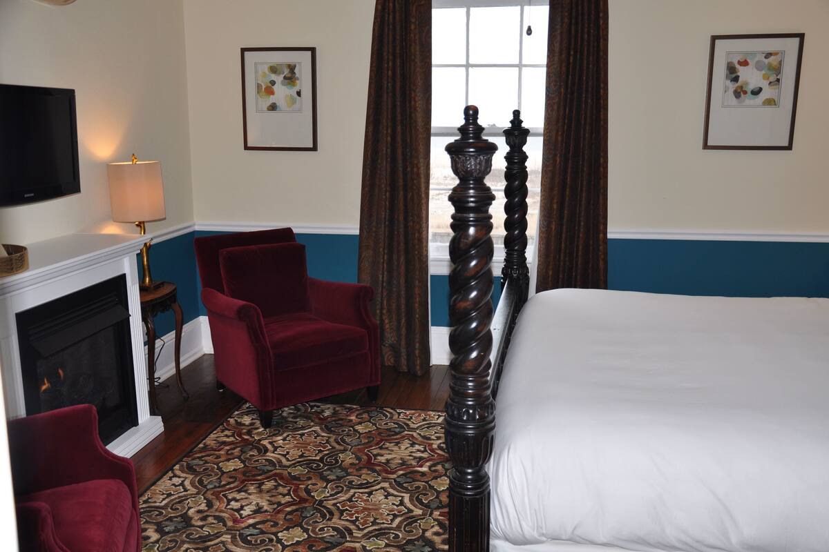 A bedroom with a large bed, a fireplace, a red armchair, and a patterned rug.