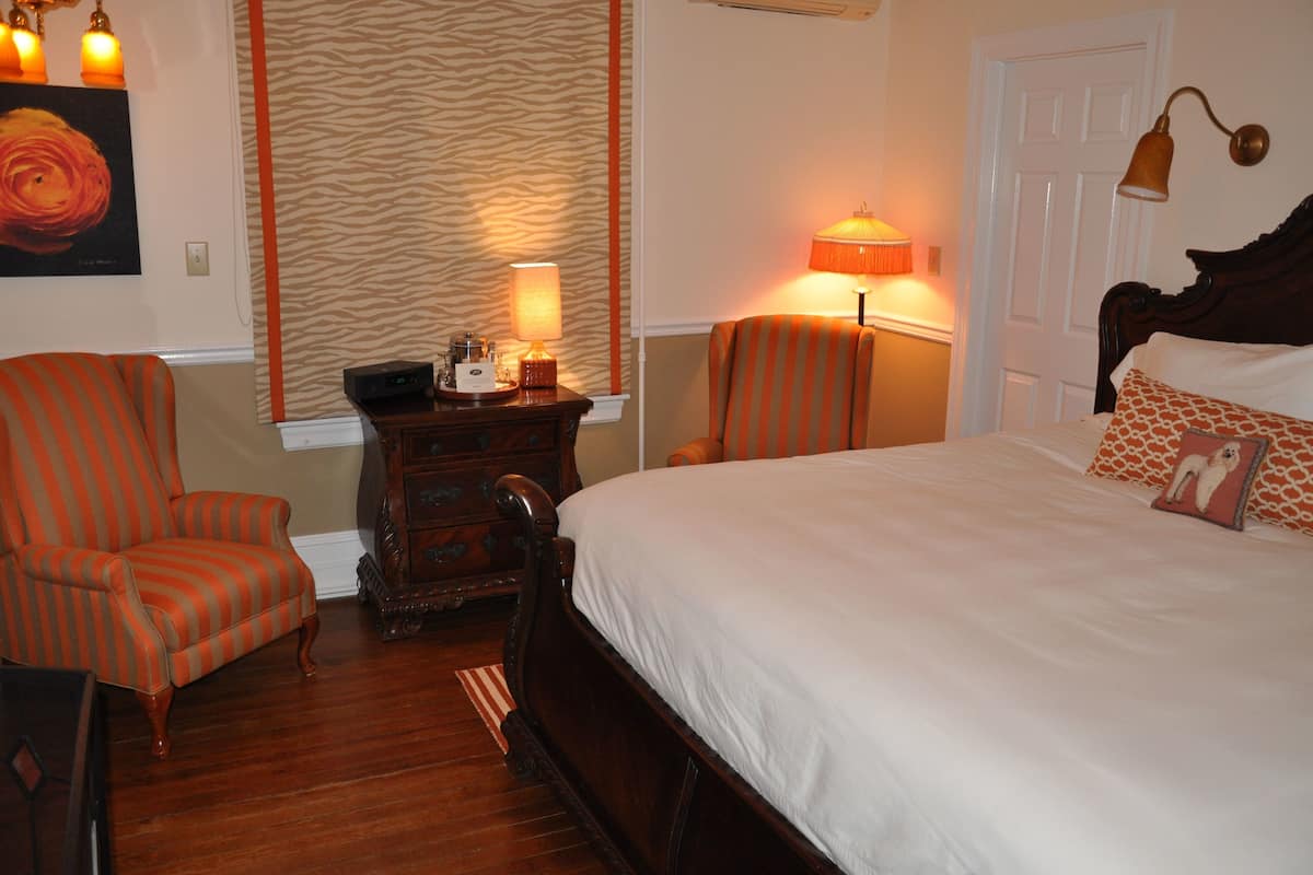 A hotel room with a large bed, two striped armchairs, a wooden nightstand, and a zebra-patterned wall.