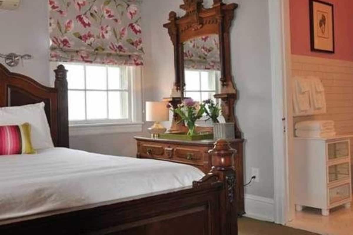 A bedroom with a wooden bed, a dresser, a mirror, and a window with floral curtains.