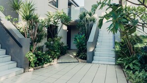 Ein modernes Gebäude mit einer Treppe, die zu einem überdachten Eingang führt, umgeben von Pflanzen und Grün.