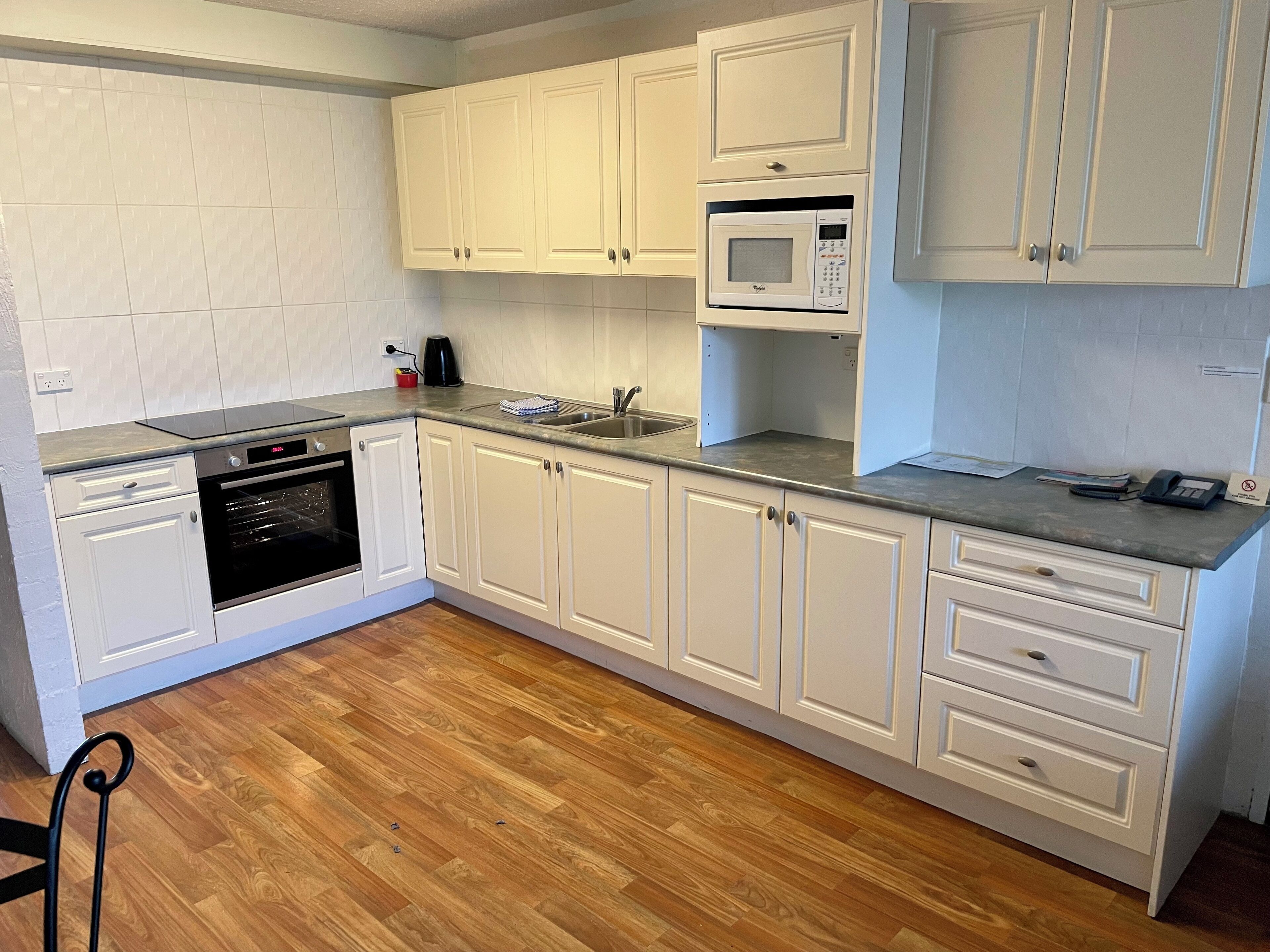 Una cocina con armarios blancos, microondas, lavaplatos y fregadero.