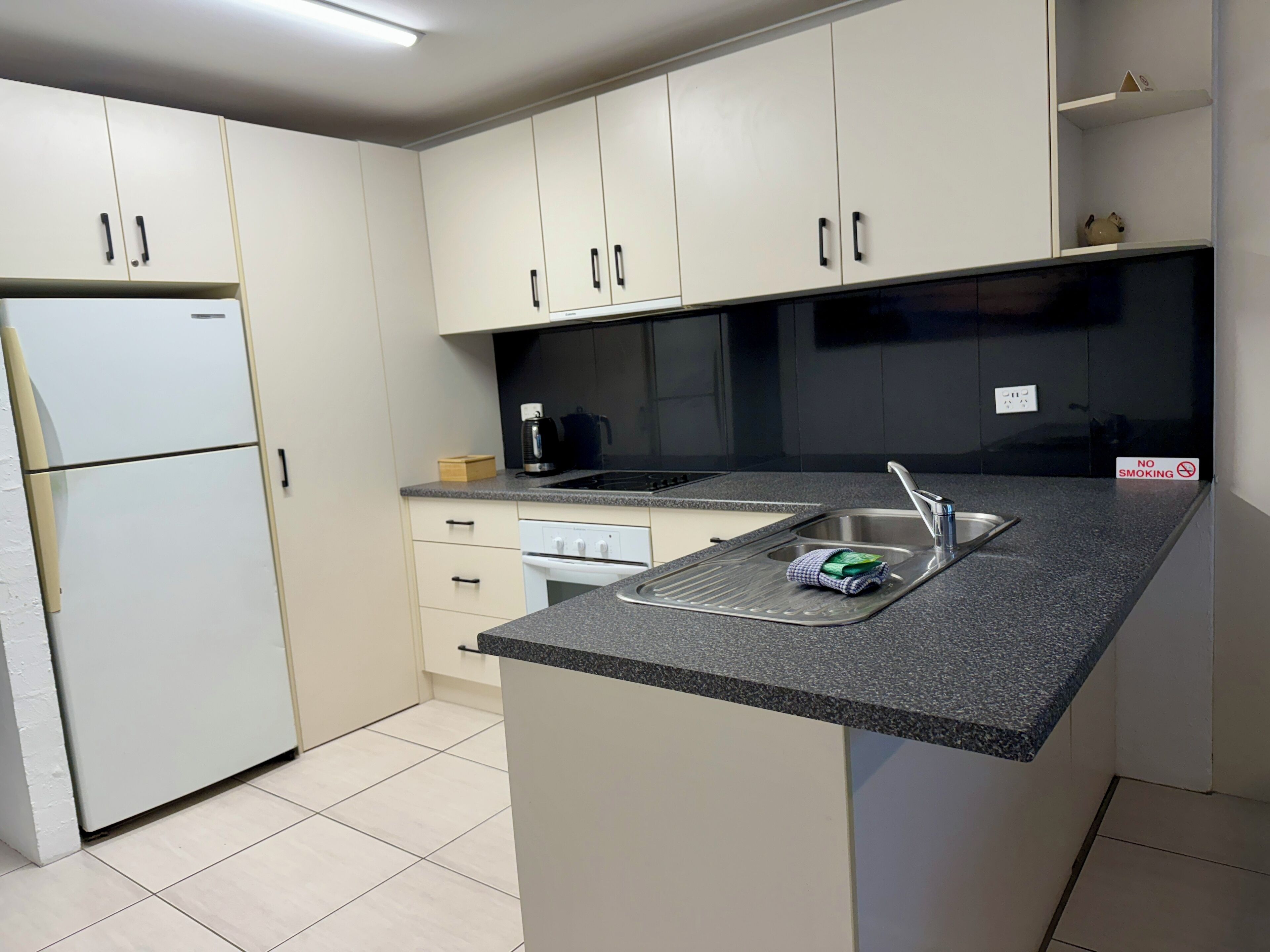 A modern kitchen with white cabinets, a built-in dishwasher, a stainless steel sink, and a coffee maker.