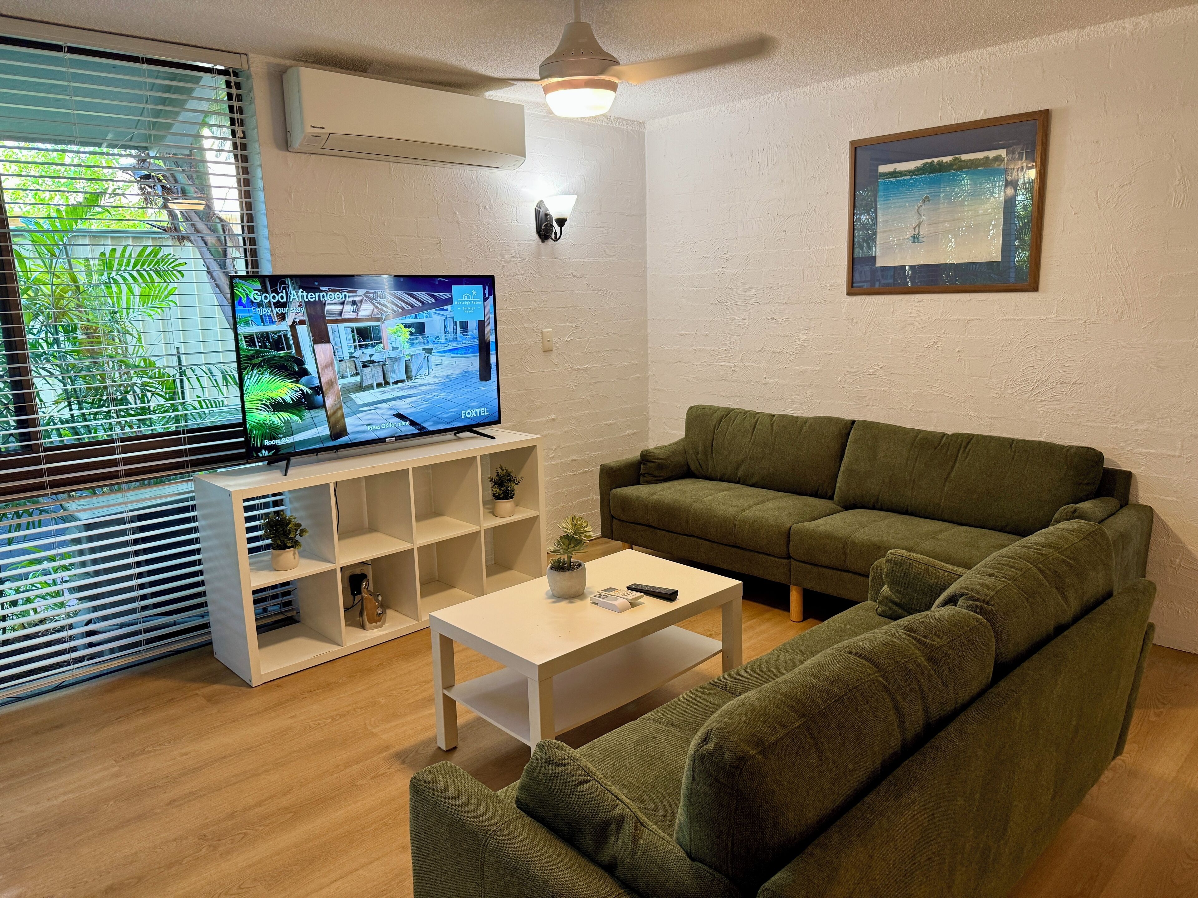 A living room with a green sofa, a white coffee table, and a TV on a stand.