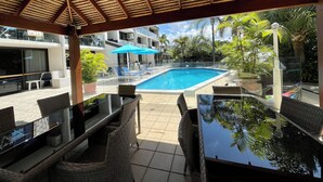 Ein überdachter Außenbereich mit Pool, Liegestühlen und Esstischen.