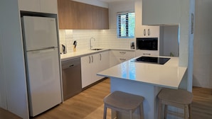 Eine moderne Küche mit weißen Schränken, einem integrierten Geschirrspüler, einem Edelstahlkühlschrank, einer Mikrowelle und einer großen Kochinsel mit Sitzgelegenheiten.