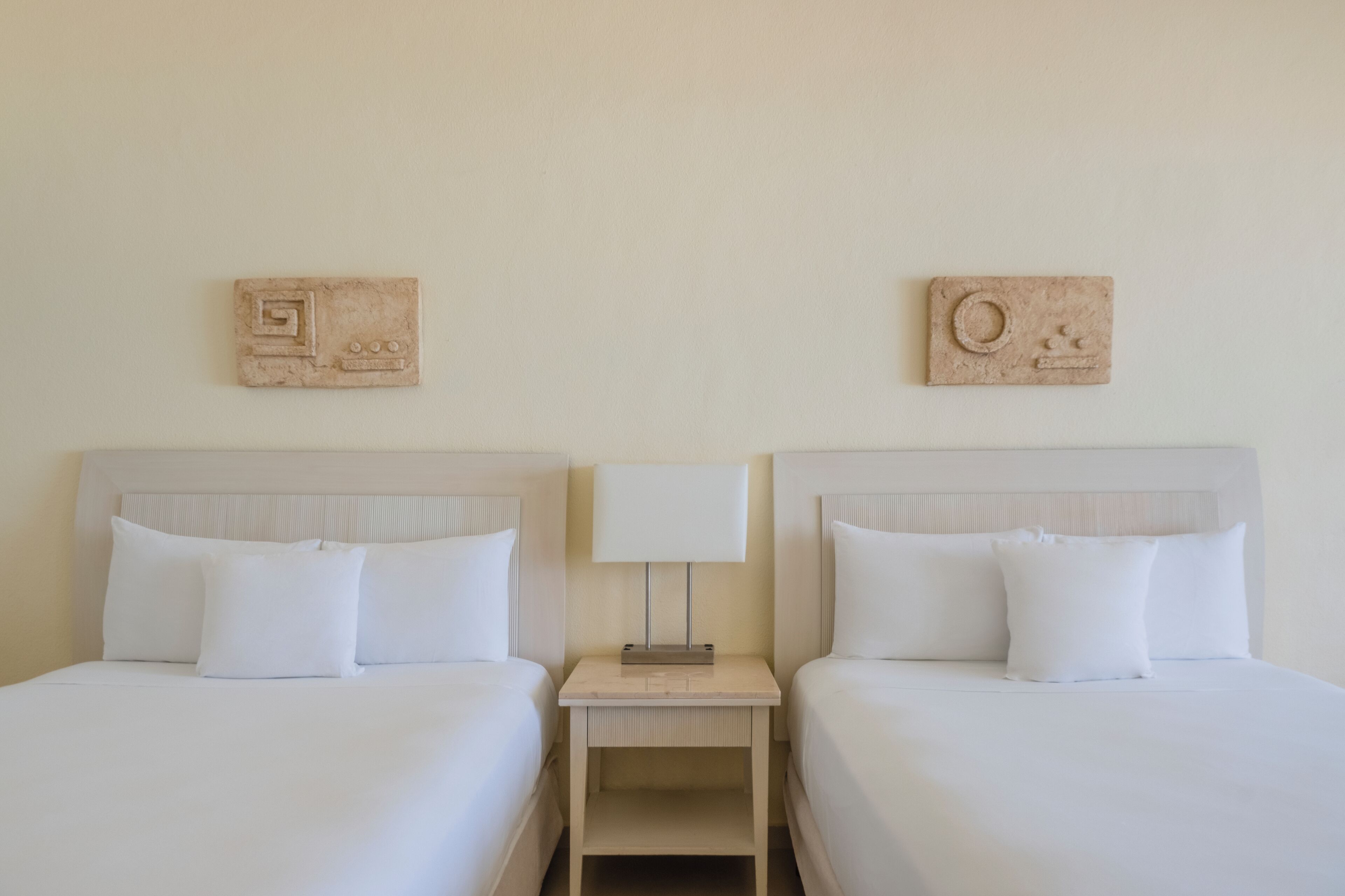 A hotel room with two beds, a nightstand, and a wall-mounted lamp.