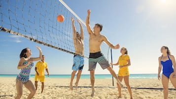 Een groep mensen speelt strandvolleybal op een zandstrand onder een heldere lucht.