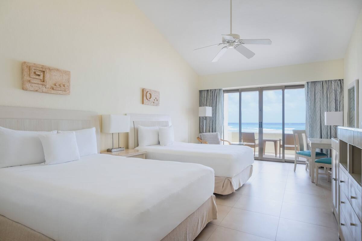 Habitación de hotel con dos camas, un escritorio, una silla y vista a la playa.