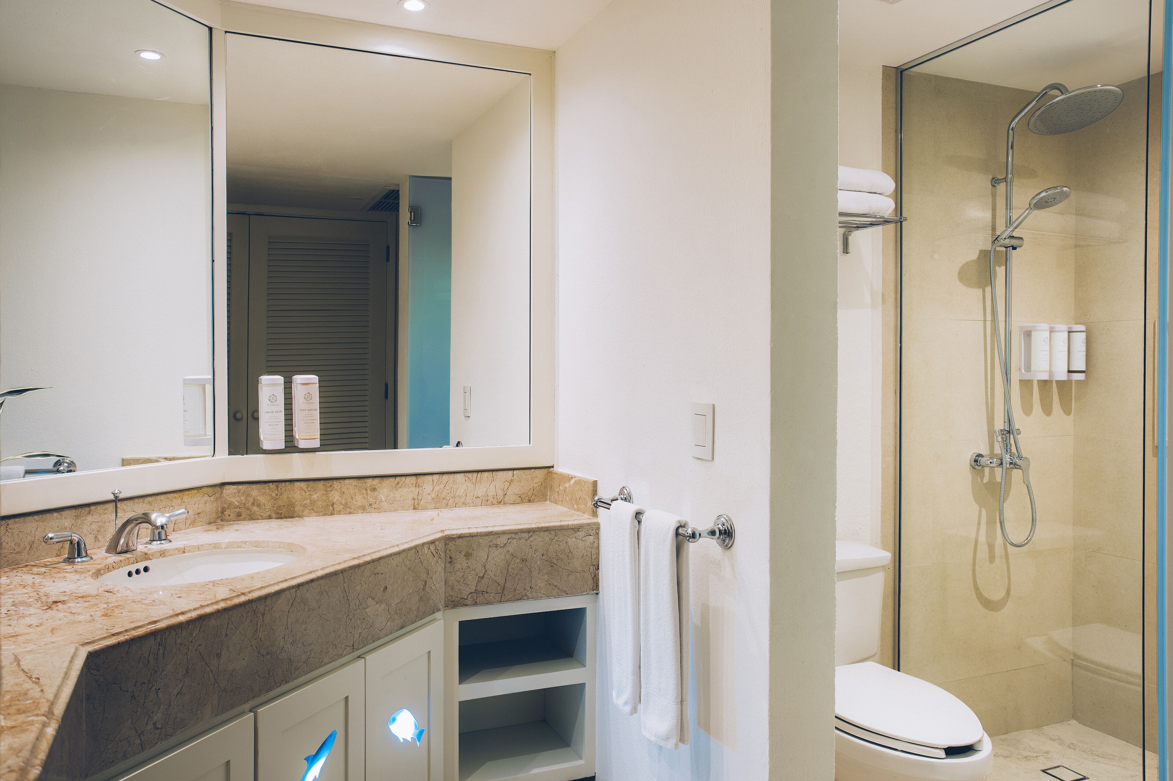 Une salle de bain moderne avec un lavabo en marbre, un grand miroir, une douche à parois de verre et des toilettes.