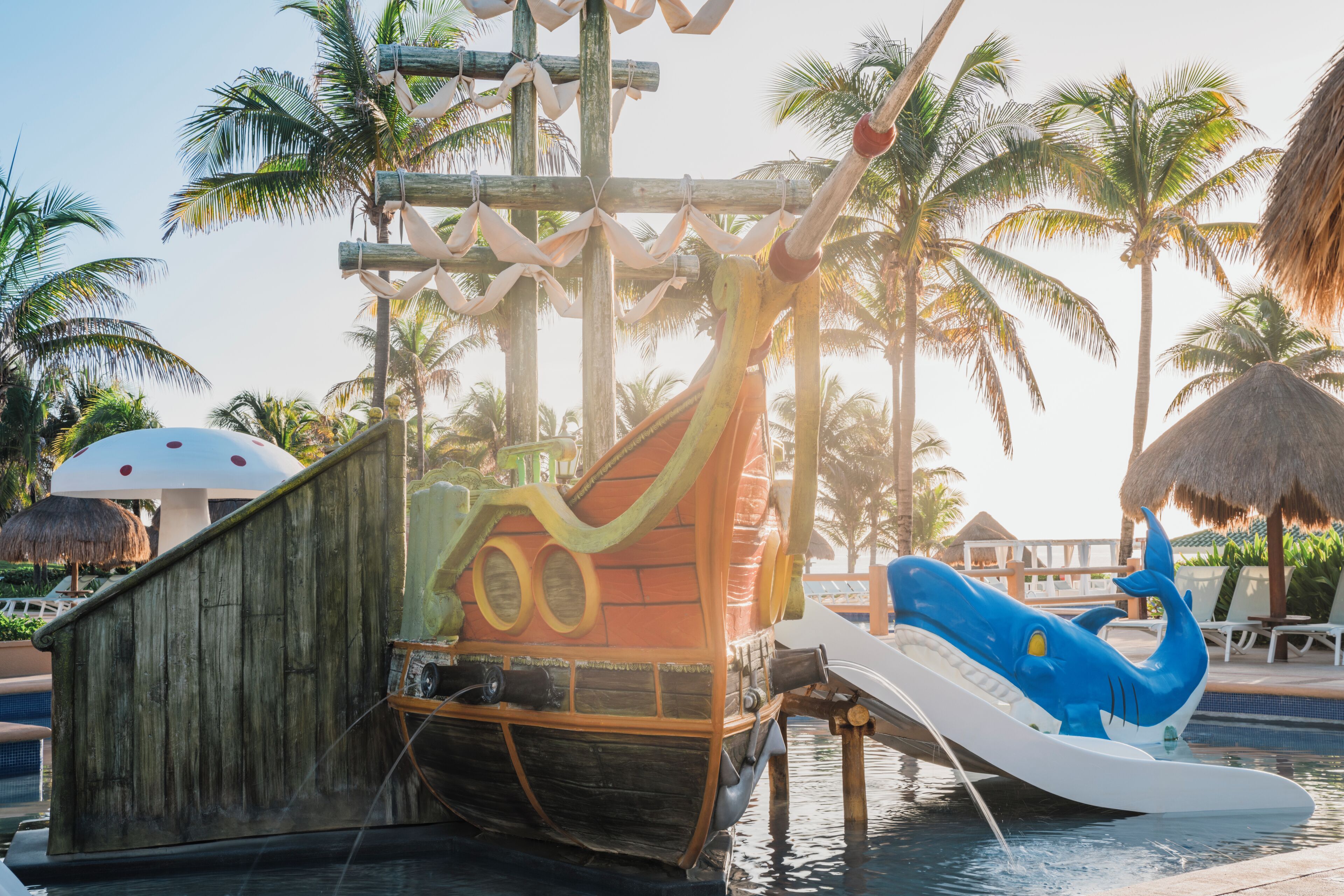 A water park with a pirate ship, a blue shark slide, and palm trees.