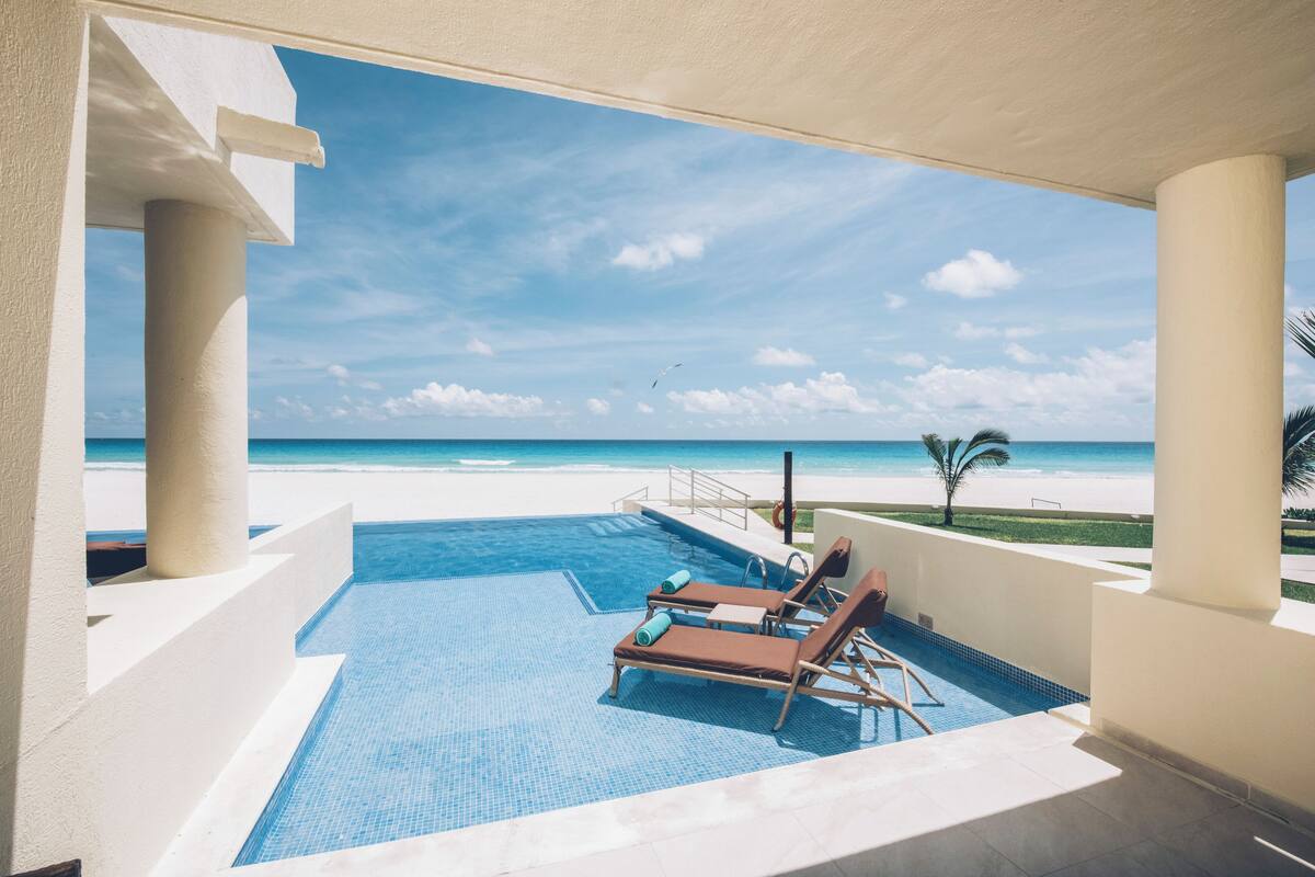 Zona de piscina con sillones de descanso y vista a la playa.