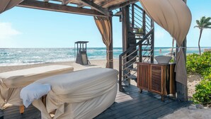 A beachside wooden structure with a covered massage table and a wooden cabinet with a bowl. - Iberostar Selection Cancún - All Inclusive (Cancun)