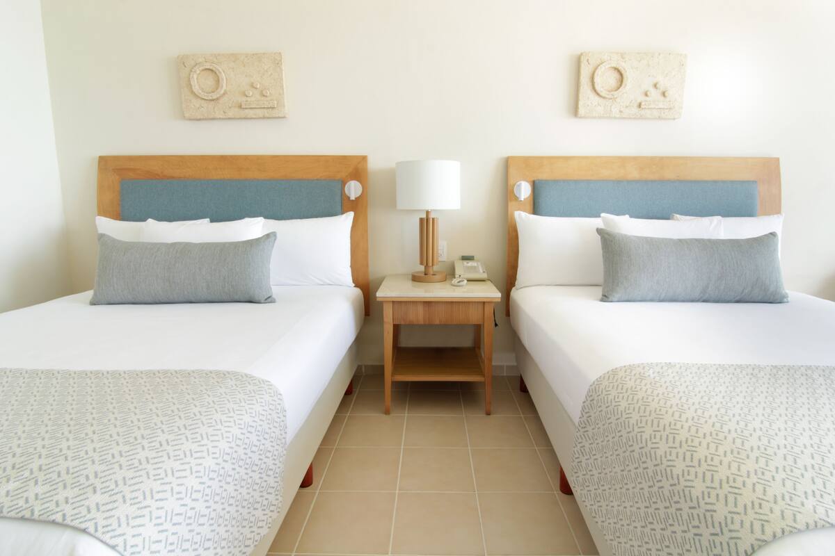 Habitación de hotel con dos camas, una mesita de noche con lámpara y decoración en la pared.
