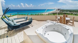 A balcony with a wicker lounge chair, a hot tub, and a table with chairs. - Iberostar Selection Cancún - All Inclusive (Cancun)
