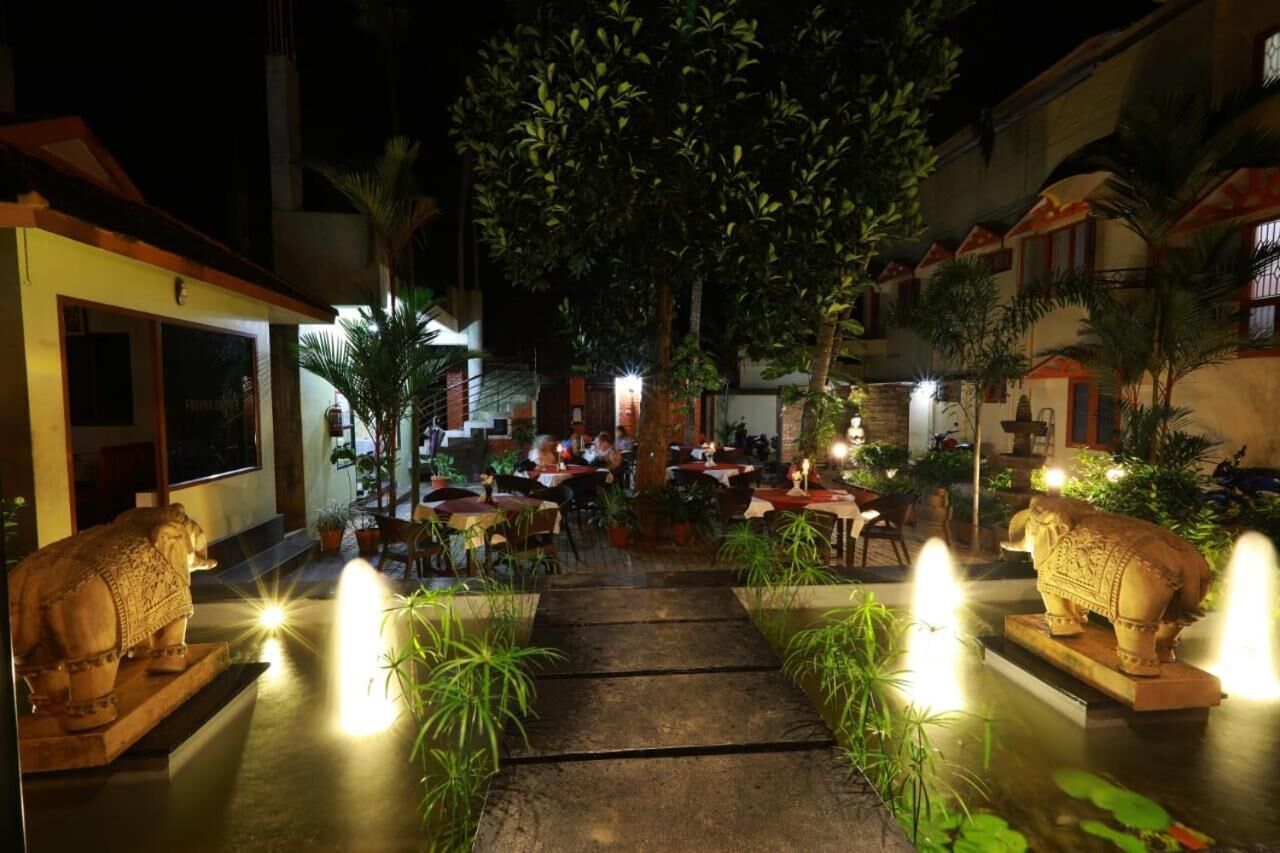 An outdoor dining area with tables and chairs, surrounded by potted plants and decorative stone elephants.