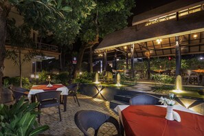An outdoor dining area with tables and chairs, a small fountain, and a covered seating area with ambient lighting. - Ideal Ayurvedic Resort (Neyyattinkara)