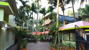Un patio con plantas en macetas, suelo de tejas rojas y un edificio con fachada verde y amarilla.