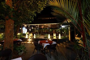 An outdoor dining area with tables and chairs, surrounded by lush greenery and a covered seating area. - Ideal Ayurvedic Resort (Neyyattinkara)