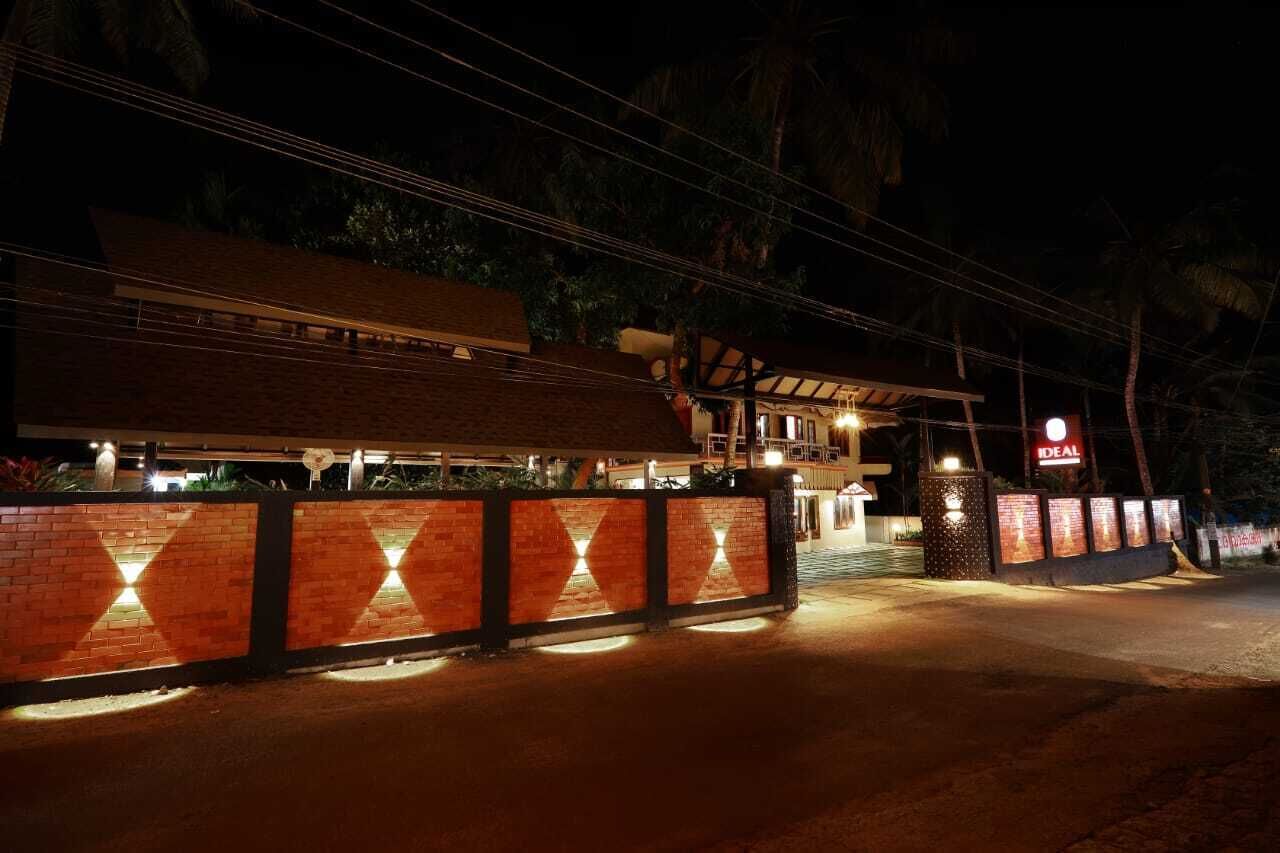 A hotel entrance at night with a brick wall, illuminated by lights, and a sign reading "IDEAL".