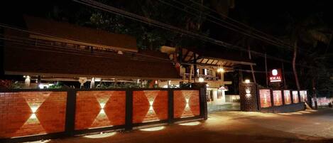 A hotel entrance at night with a brick wall, illuminated by lights, and a sign reading "IDEAL".