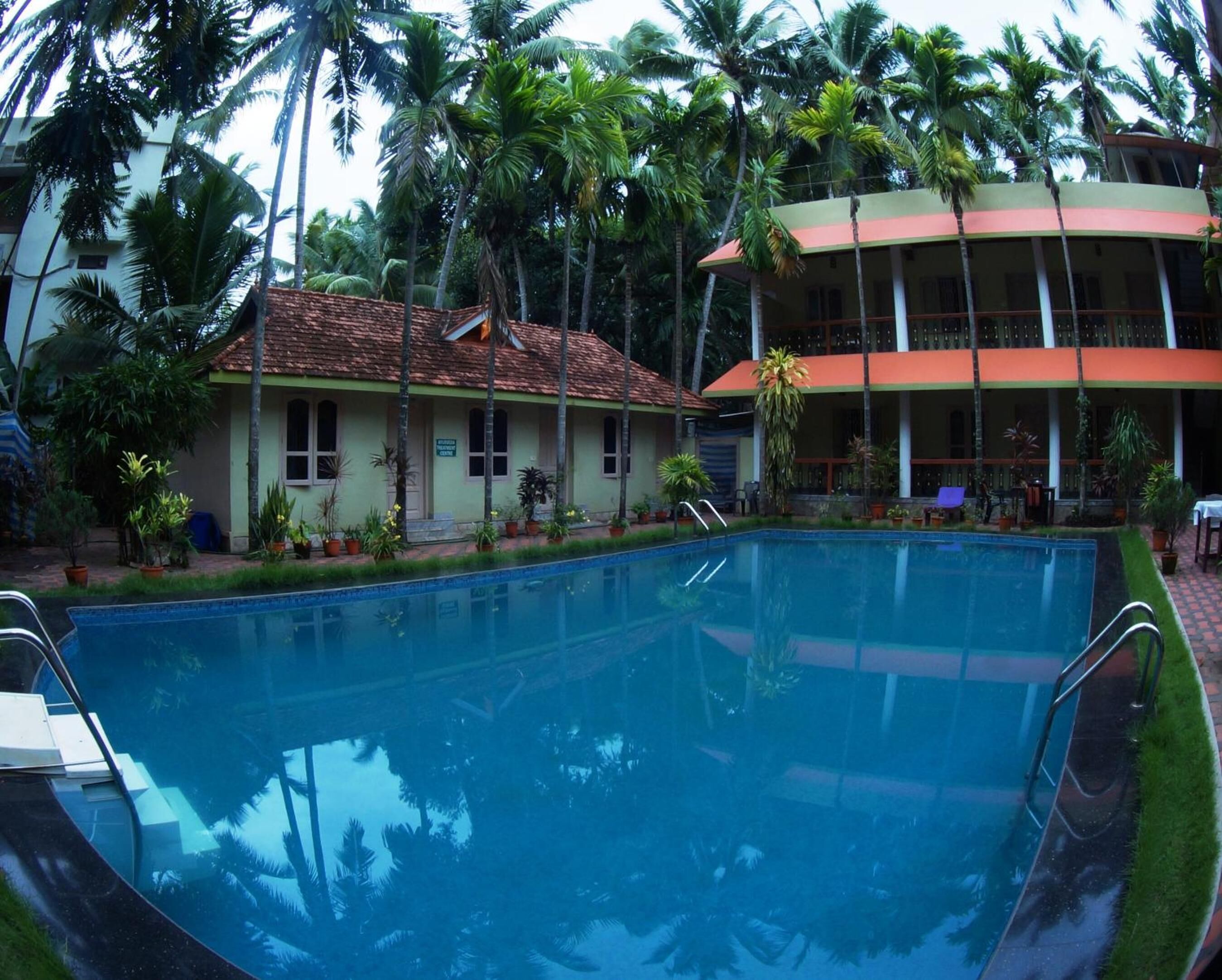A swimming pool surrounded by lush greenery and a building with a tiled roof.