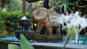 Una estatua de piedra de un elefante con un elemento acuático en un jardín.