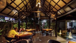 Un área de comedor al aire libre con mesas y sillas, rodeada de plantas y una fuente.