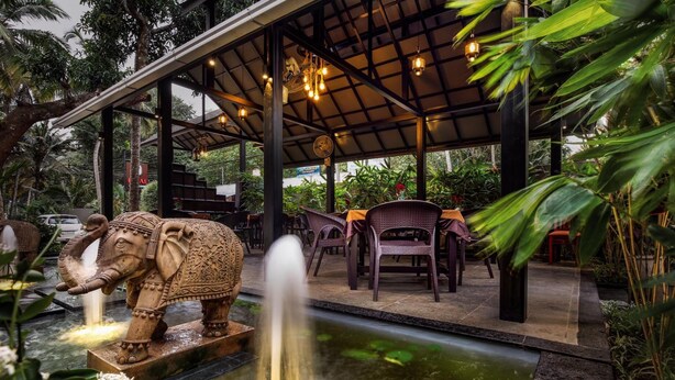 Un espacio de estar al aire libre con una fuente, rodeado de abundante vegetación y una estatua decorativa de un elefante.