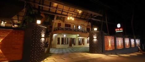 Entrada de un hotel con un vestíbulo cubierto, un letrero que dice “IDEAL” y una fachada bien iluminada.