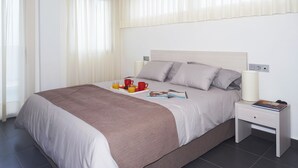 Una cama bien hecha con una manta marrón, una mesita de noche con una lámpara y una bandeja con jugo de naranja y vasos rojos.