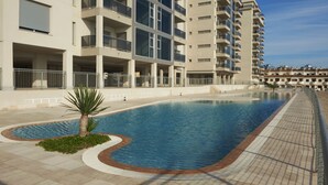Un hotel moderno con piscina, varios balcones y cielo despejado.