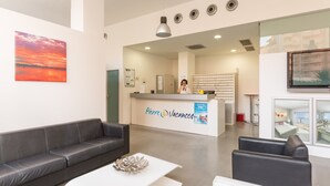 Un área de recepción moderna con un sofá gris, una mesa de centro blanca y un mostrador de recepción con la leyenda "Pierre & Vacances".