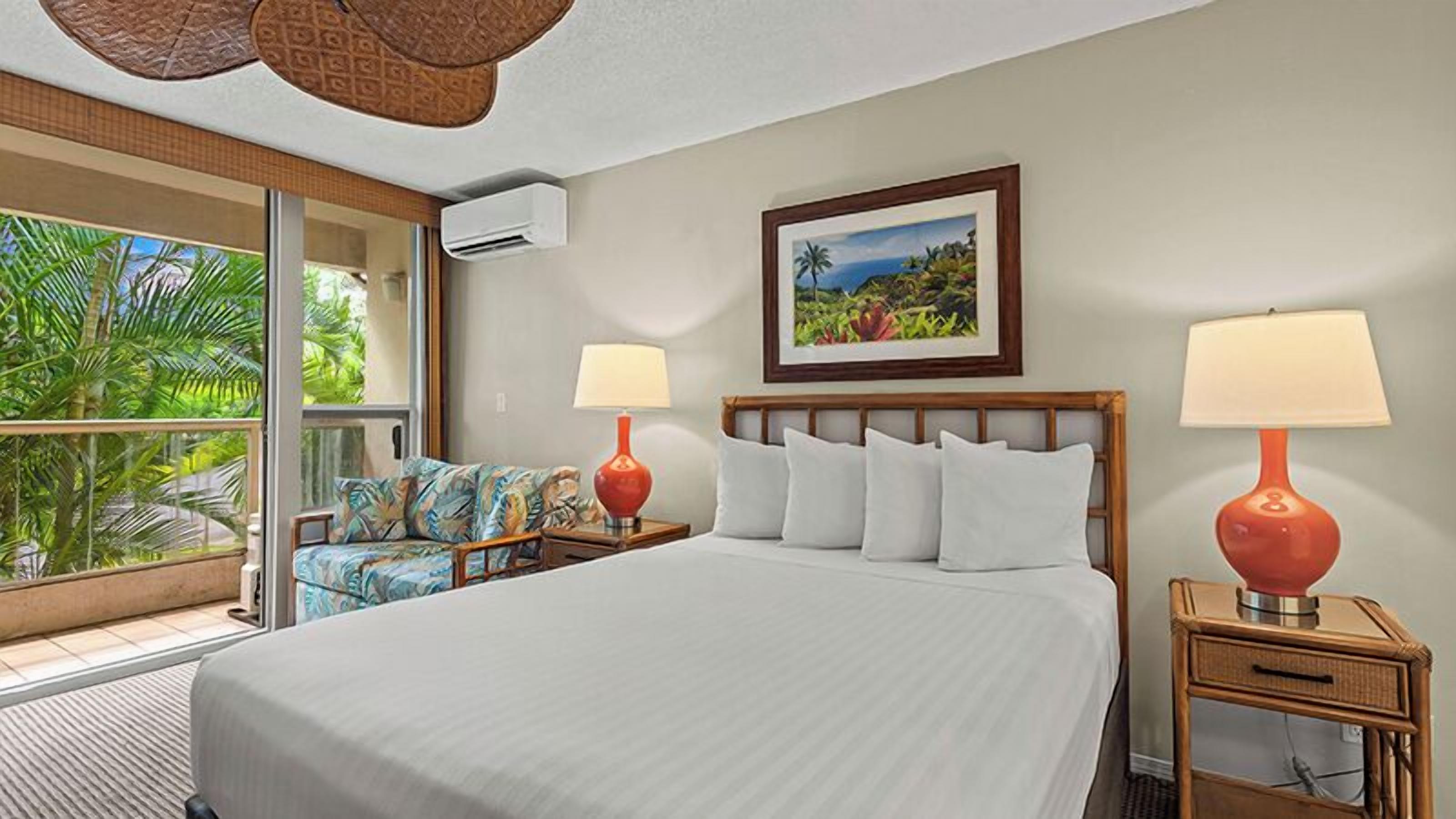 A hotel room with a large bed, two bedside tables with lamps, a window with a view of palm trees, and a painting on the wall.