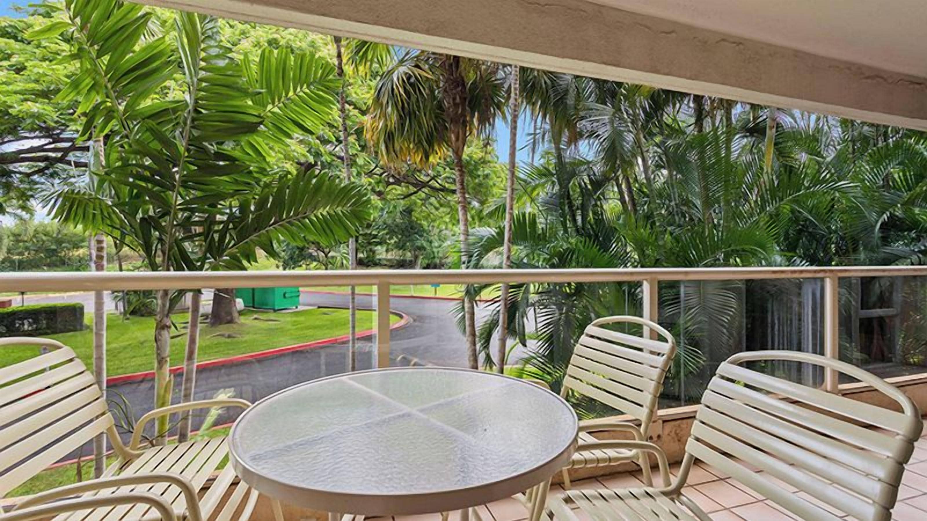 A balcony with a round table and four chairs, overlooking a road and greenery.