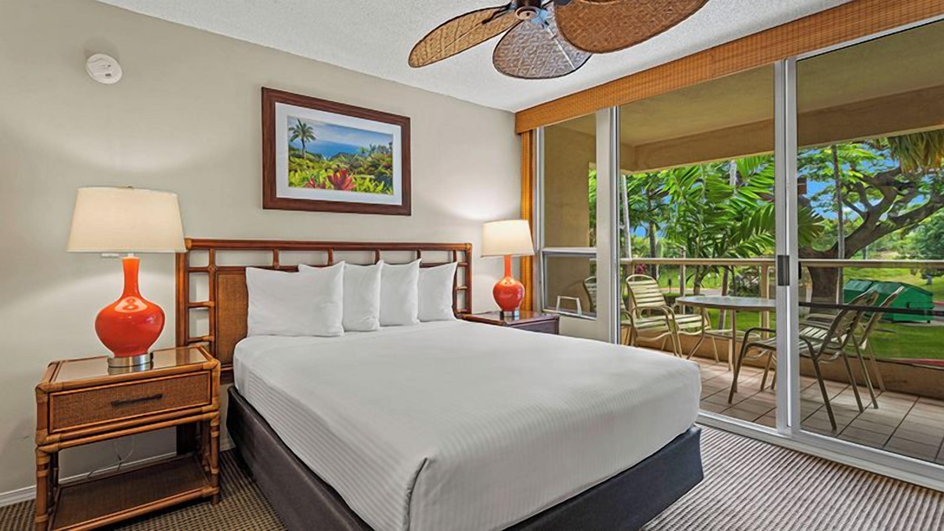 A hotel room with a large bed, two bedside lamps, a picture on the wall, and a balcony with chairs.