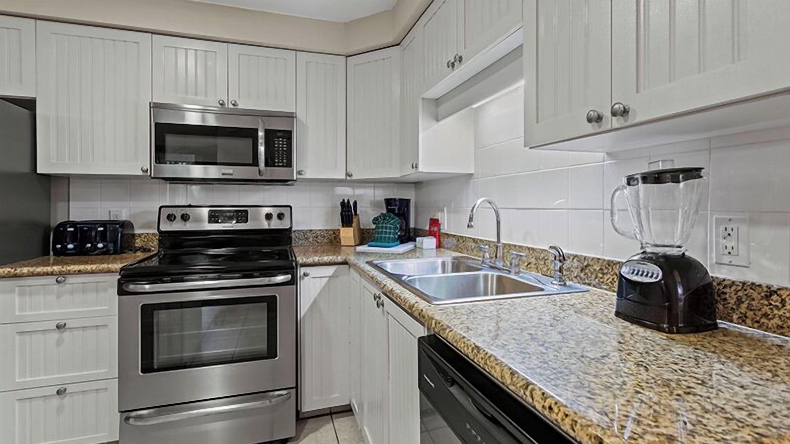 Una cocina con electrodomésticos de acero inoxidable, encimera de granito y armarios blancos.
