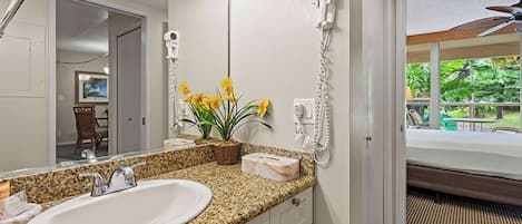 A bathroom with a granite countertop sink, a hairdryer, and a window with a view of greenery.