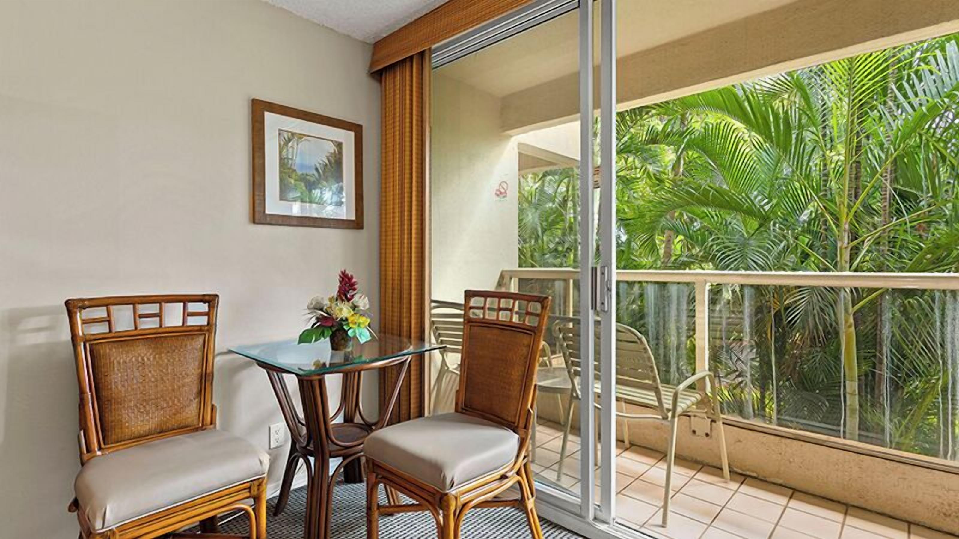Un balcon avec des fauteuils en osier, une table en verre et une vue sur la végétation tropicale.